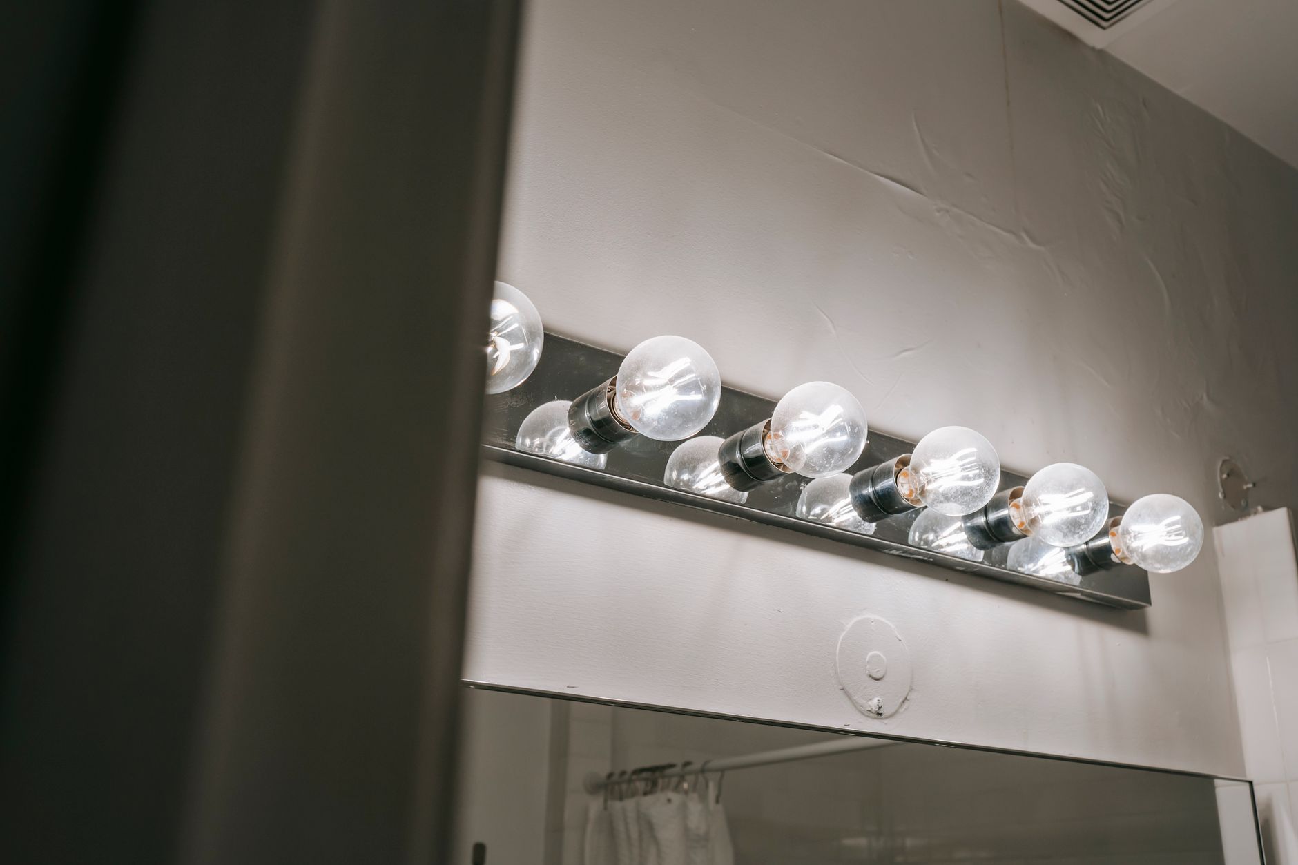 Glowing round shaped lamps reflecting on metal beam on white wall above mirror in bathroom
