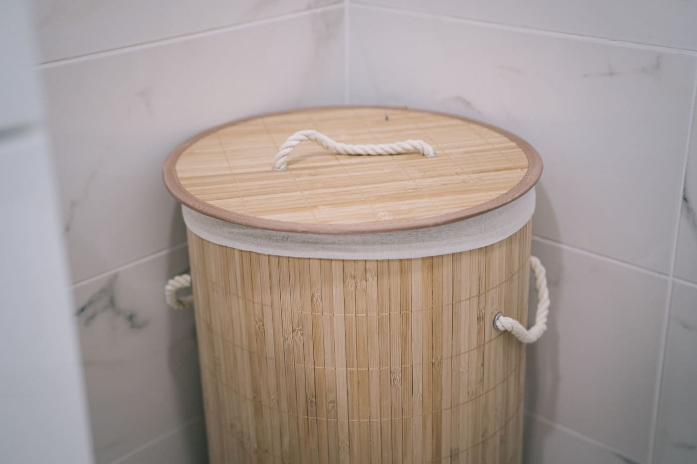 Lidded bamboo laundry hamper against a white tiled wall
