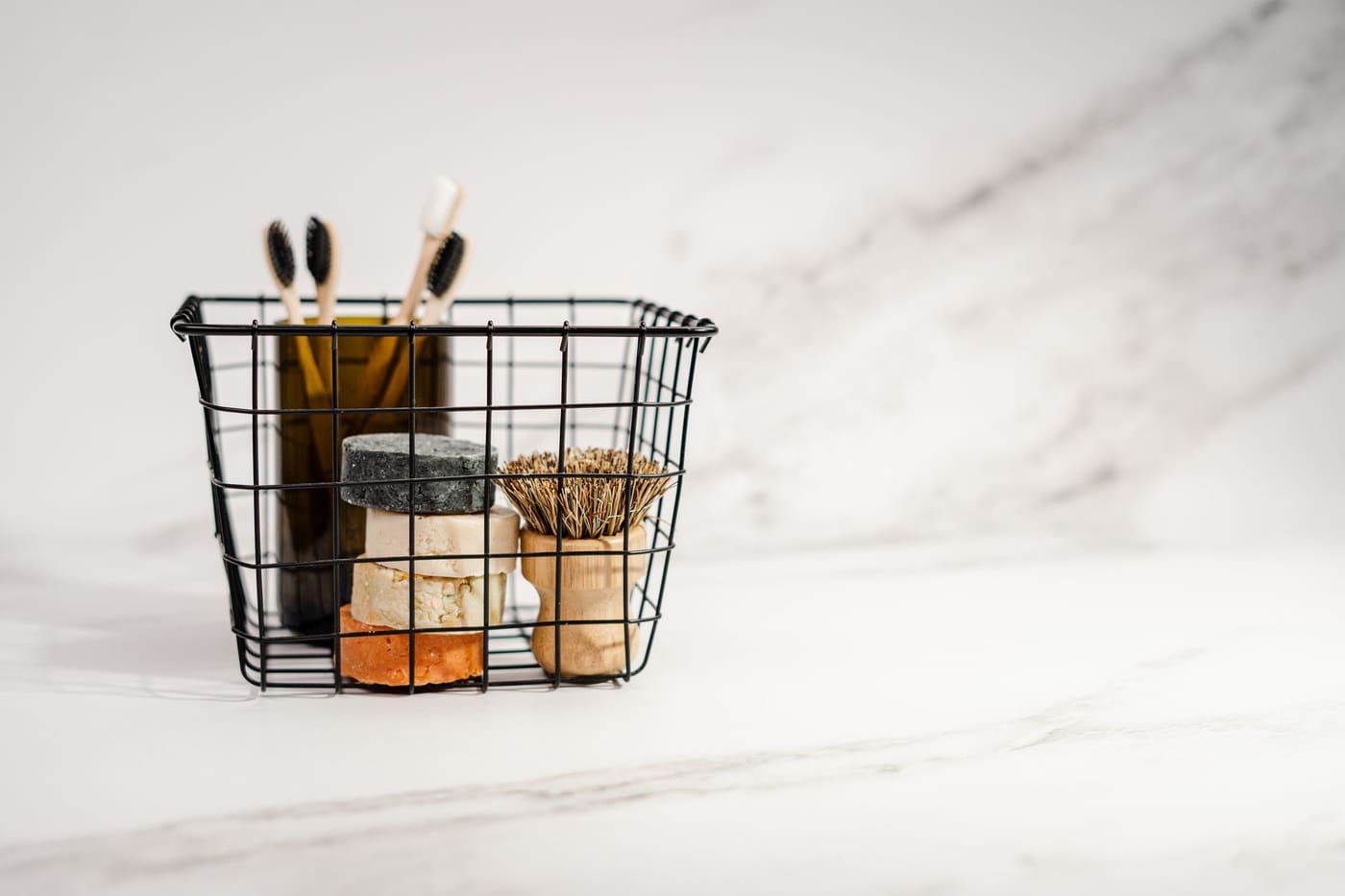 Black wire basket holding toothbrushes and small toiletries on a marble surface