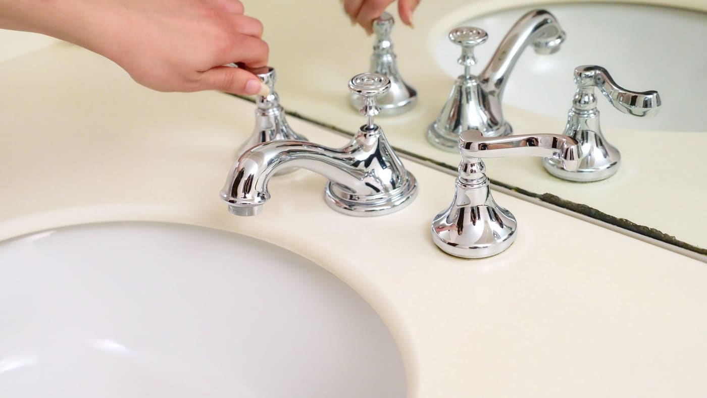 Hand adjusting a polished chrome bathroom faucet