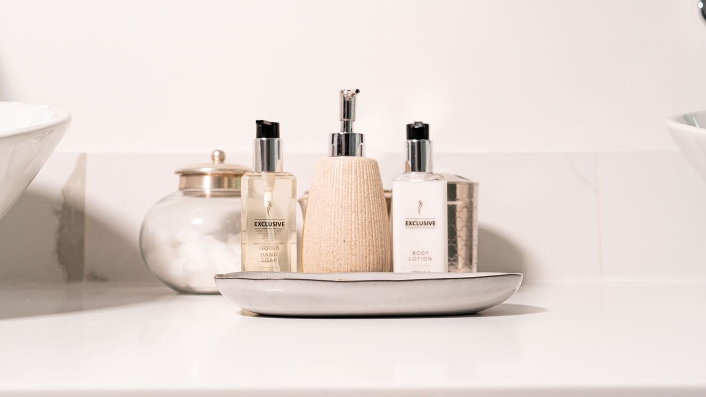 Soap and lotion bottles and a glass jar on a small tray on a white counter
