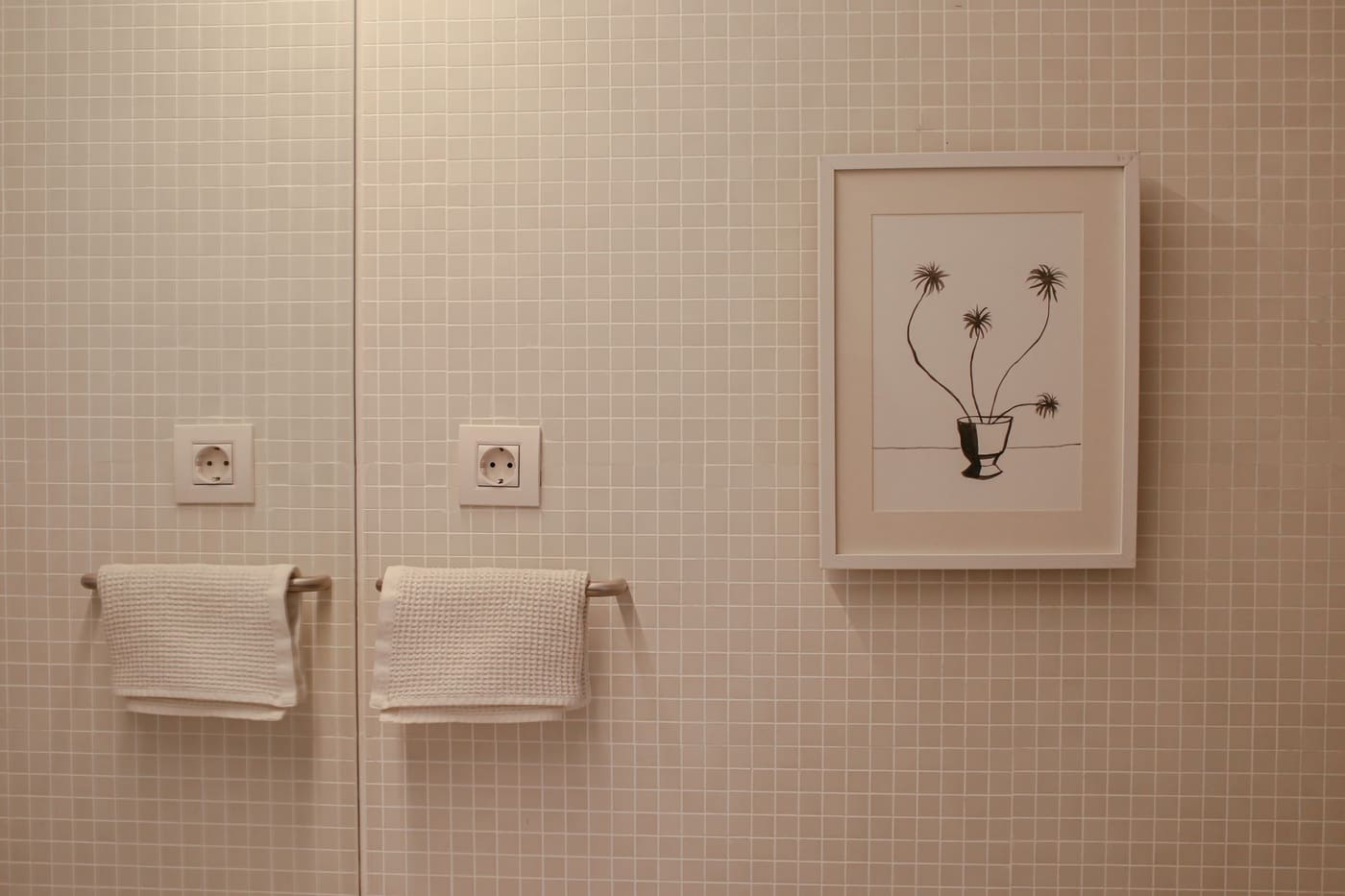 Framed botanical print on a tiled wall beside two towels on bars