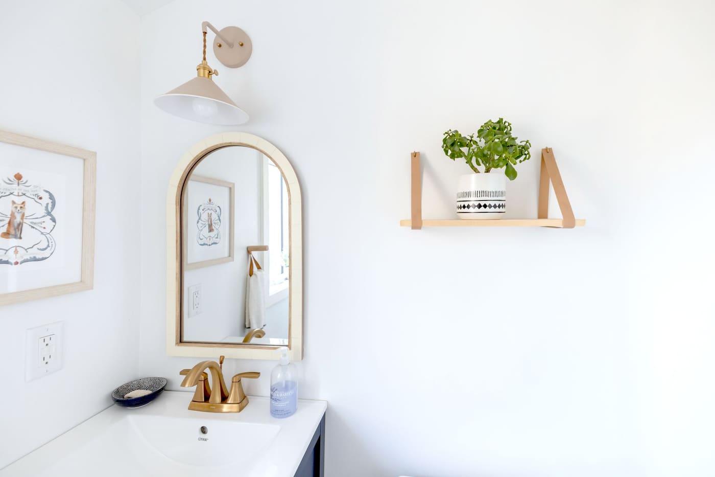 Bathroom with an arched gold mirror and a wall sconce lit above the vanity