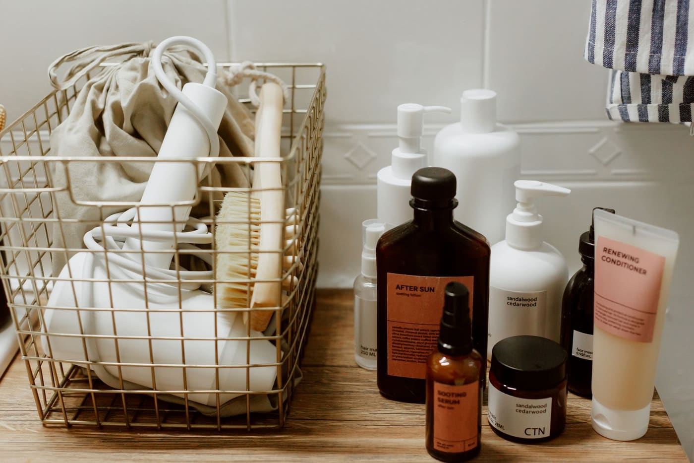 Gold wire basket holding bath products beside bottles on a wooden shelf