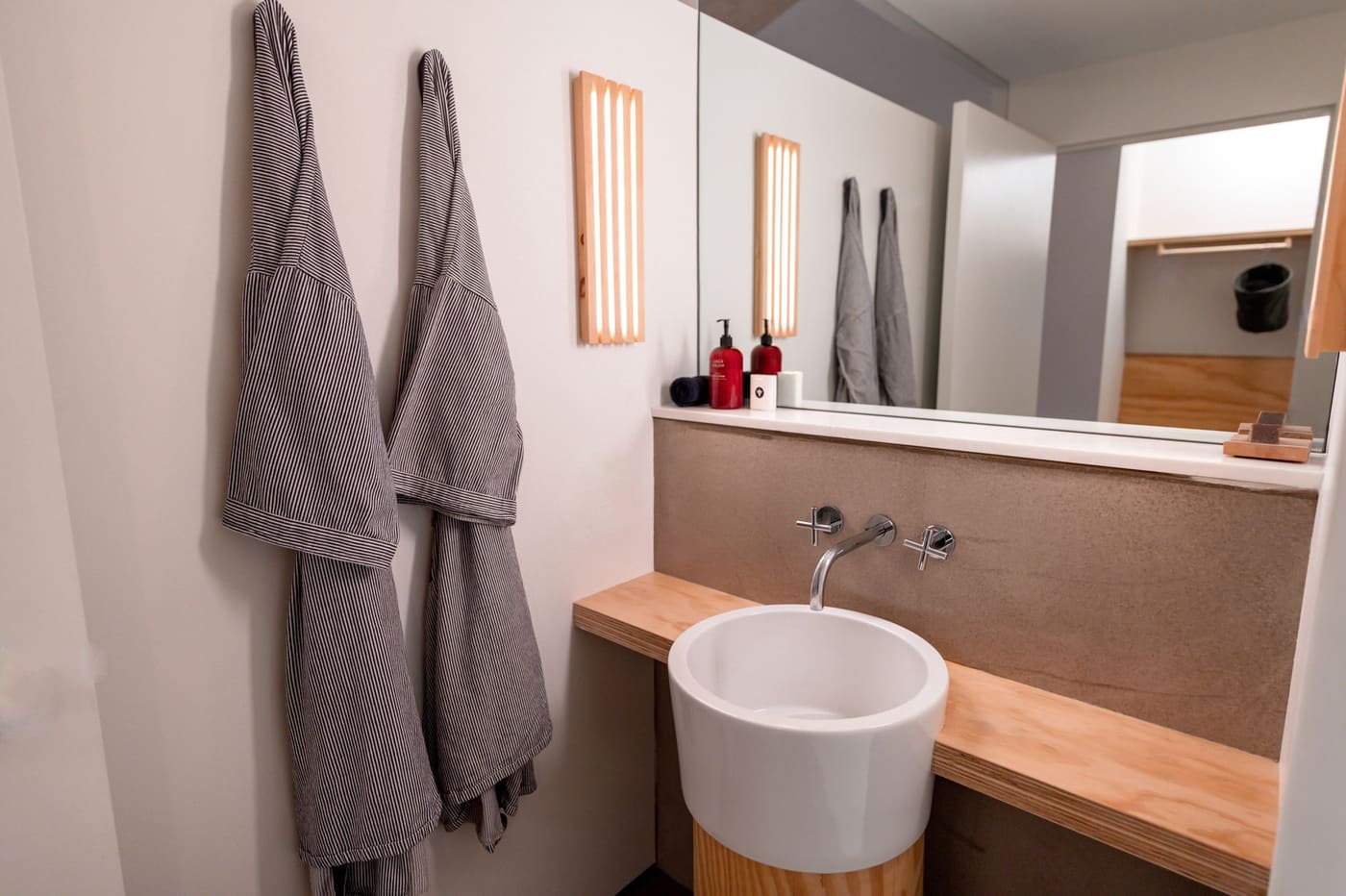 Grey towels hanging on hooks beside a round bathroom sink