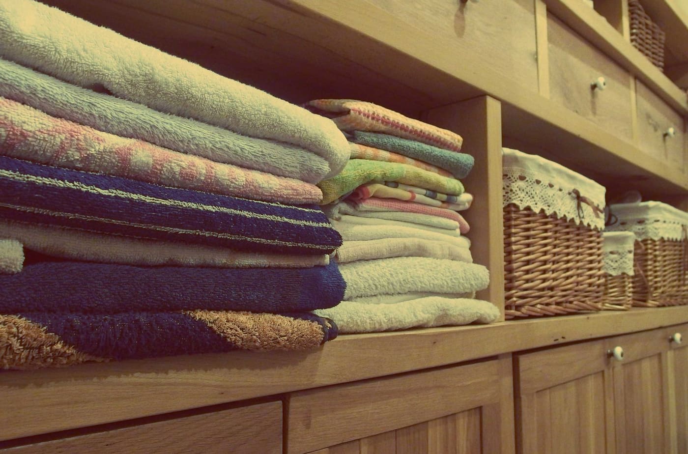 Wooden cabinet with neatly stacked folded towels and wicker baskets