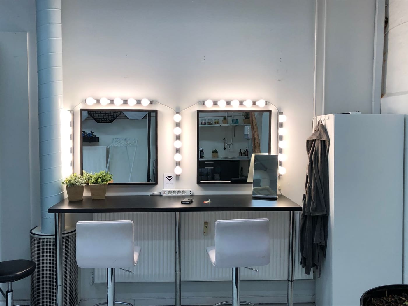 Two vanity mirrors framed with round bulbs above a counter in a bright room