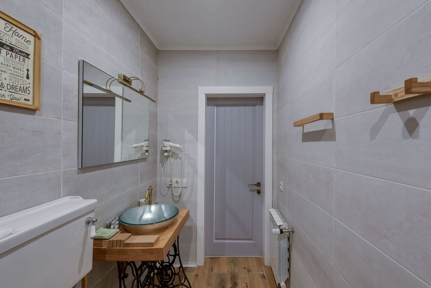 Narrow bathroom with a wooden vanity, a wall mirror and wooden towel shelves
