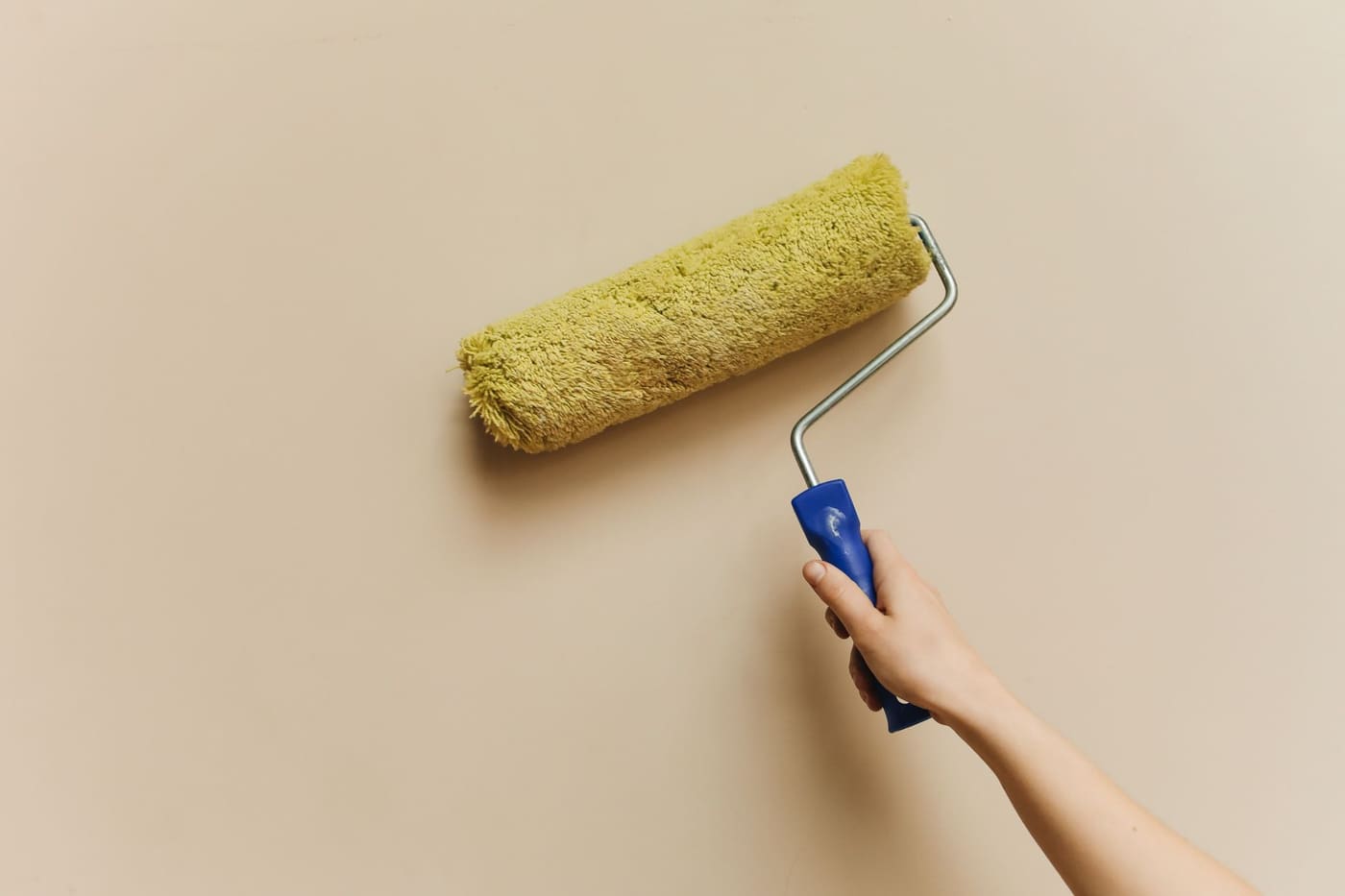 Yellow paint roller on a beige wall