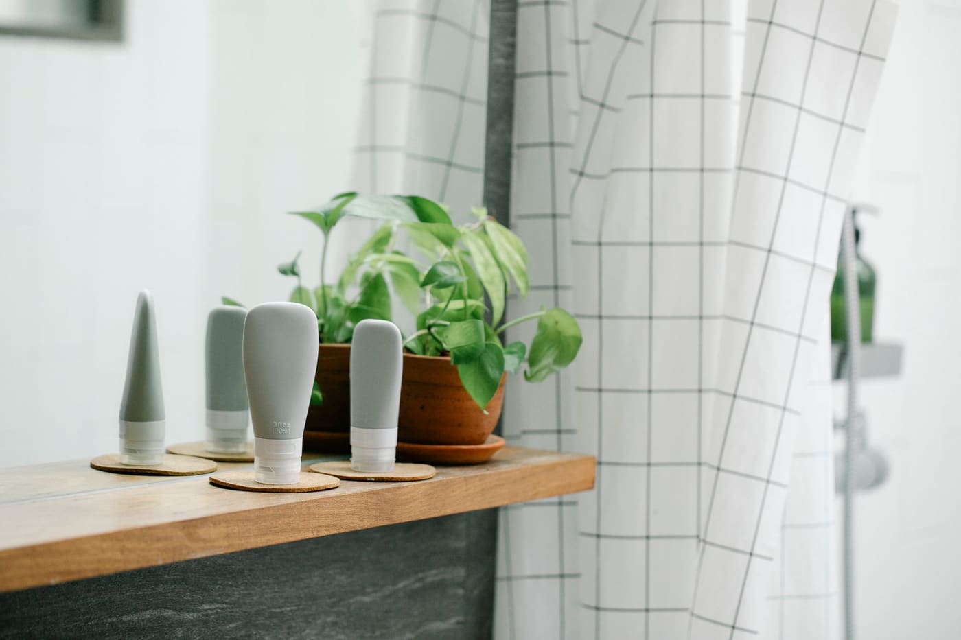 Wooden shelf with matching soap bottles and a potted plant beside a shower curtain