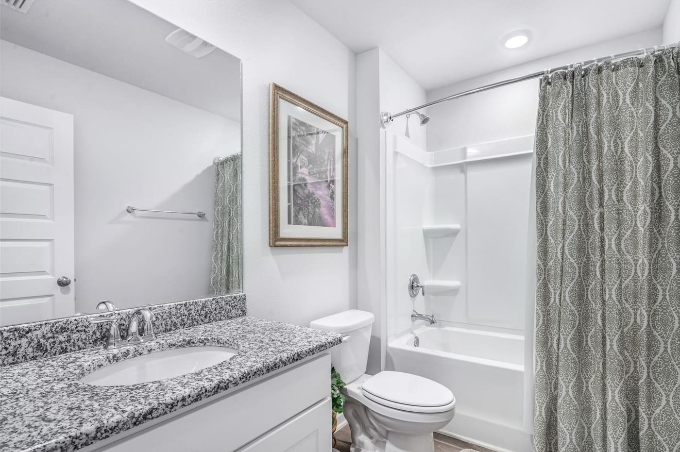 Small rental bathroom with a tub, patterned fabric shower curtain, granite vanity and a framed print