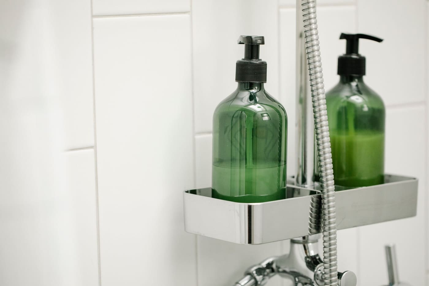 Chrome shower caddy holding two green pump bottles beside a hand shower