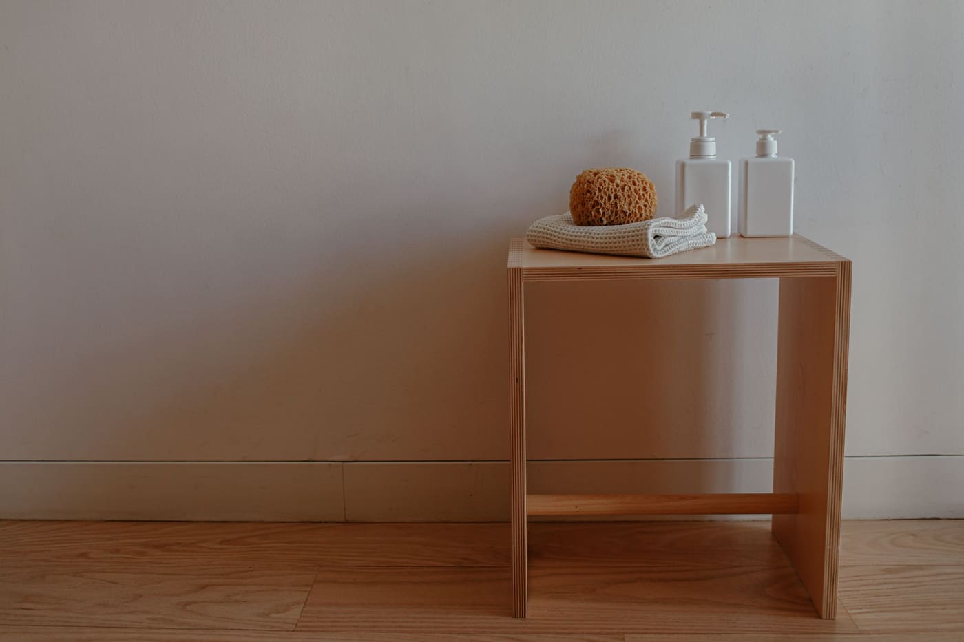 Small wooden stool holding a sponge, folded washcloth and two pump bottles