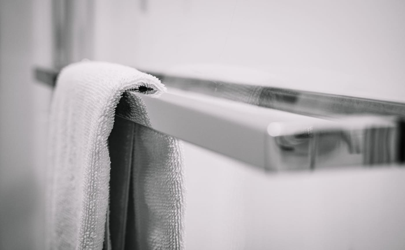 A white towel hanging straight on a chrome towel rack