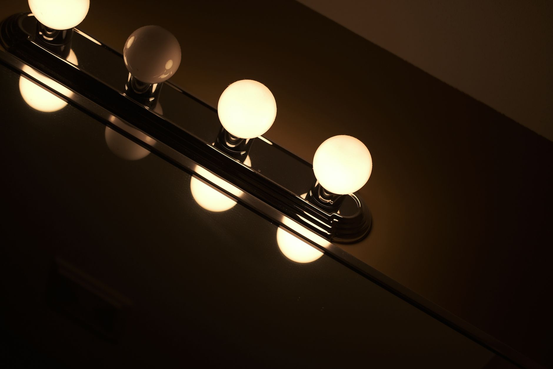 Contemporary bathroom light fixture with glowing bulbs reflecting off a mirror.